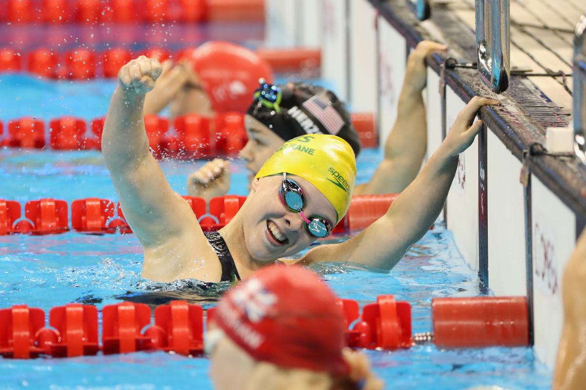 A female Para swimmer celebrating with your hand in the air between two other swimmers