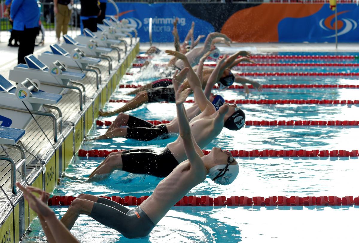 A group of male swimmers jumping in the water for a backstroke race