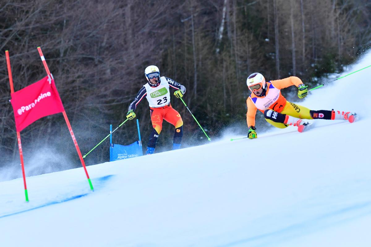 Male alpine skier making a turn with his guide behind him