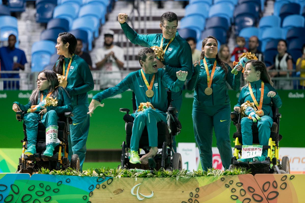 Six people on a podium. Three are in wheelchairs, three are standing behind them