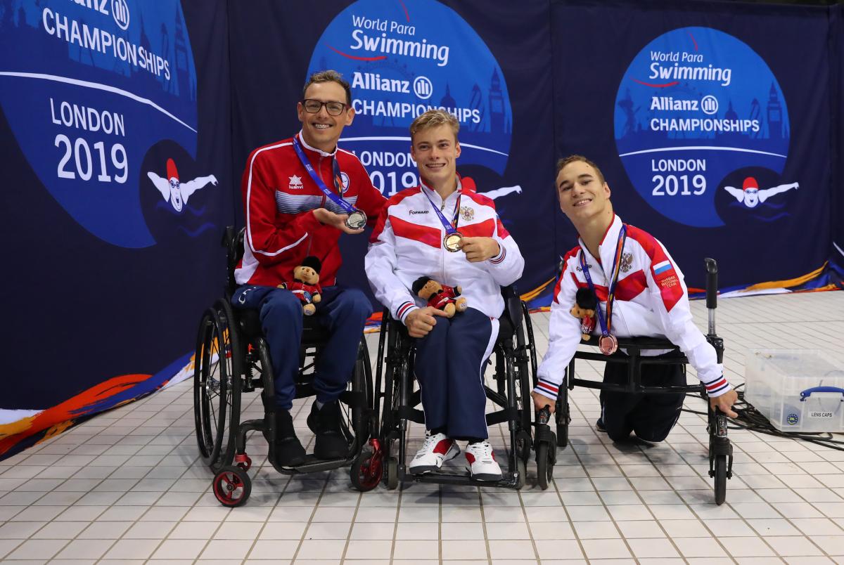 Three men in wheelchairs showing their medals