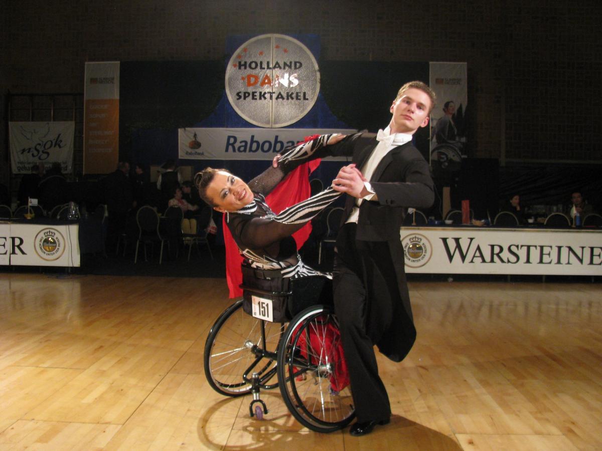 A standing man dancing with a woman in a wheelchair