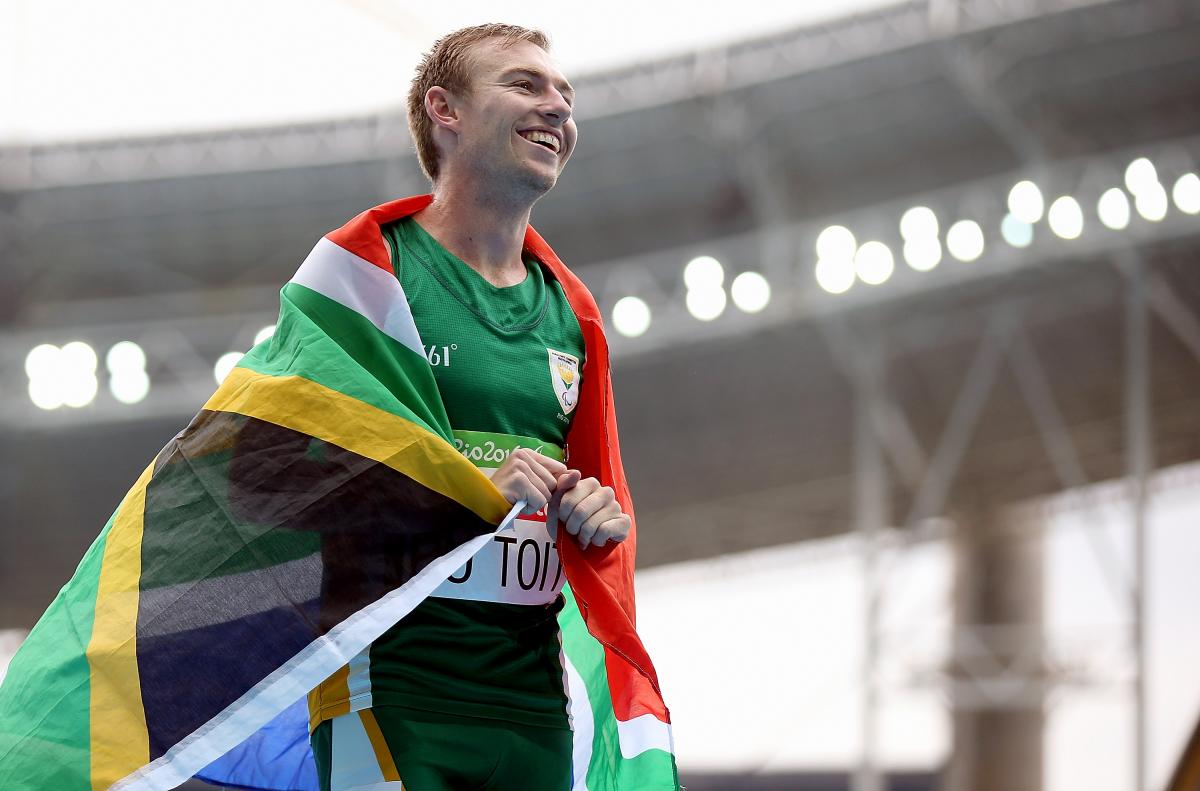 A smiling man with the flag of South Africa around his shoulders 