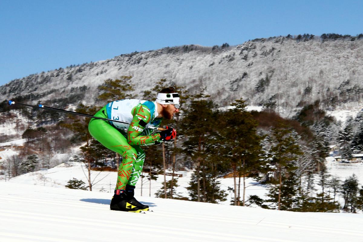 A man skiing wearing a green outfit and sunglasses