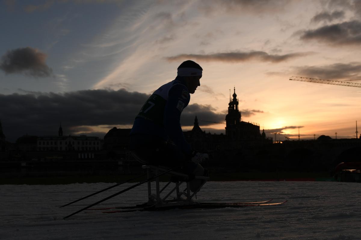 A male sit-skier competing on the snow with the Dresden skyline as background
