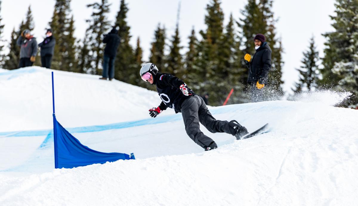 A male Para snowboarder competing being observed by three people