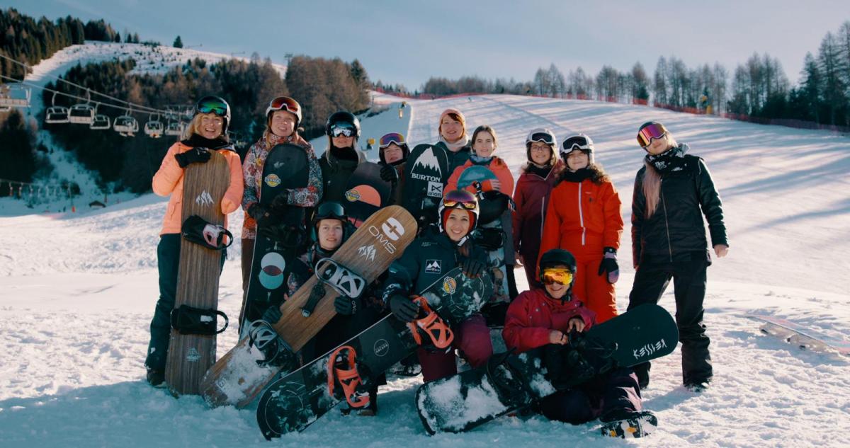 A group of 12 female Para snowboarders posing for picture with their equipment on the snow