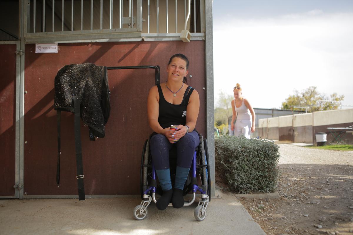 Woman in wheelchair smiles outside a horse stable
