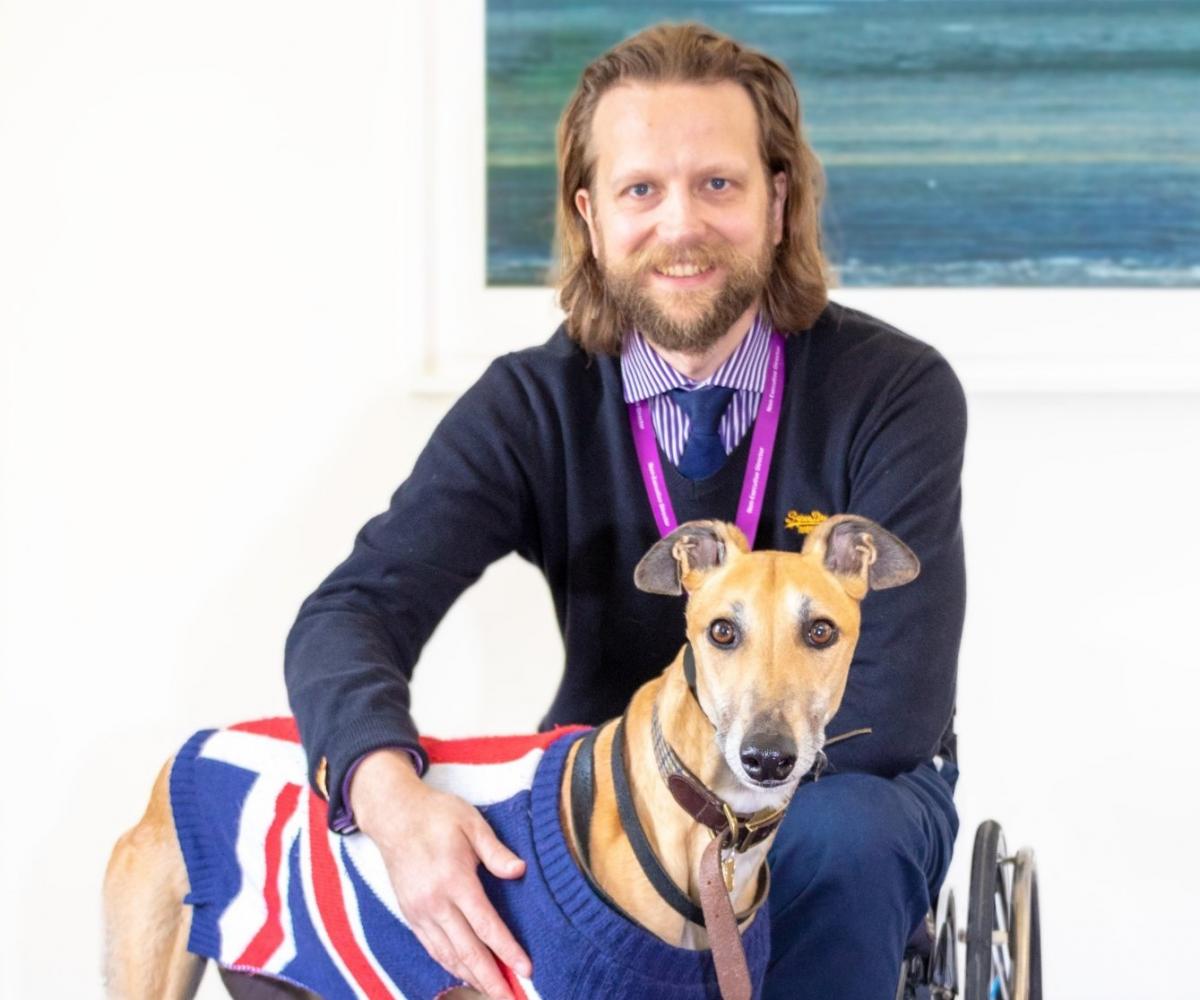 Male wheelchair user poses with his dog in a UK flag sweater