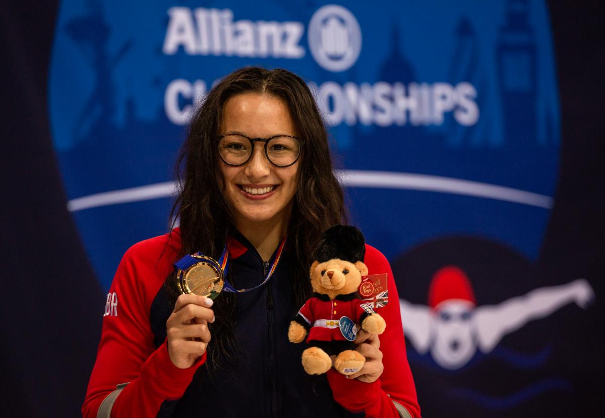 A woman wearing glasses showing her gold medal 