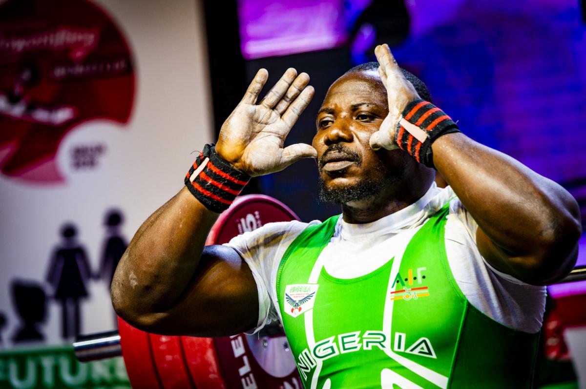 A male powerlifter with his hands in front of the face and a bar with discs behind him