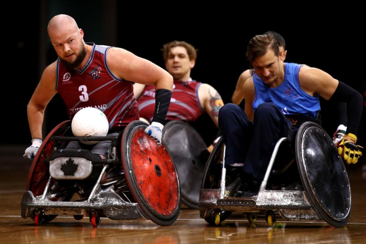 Male wheelchair rugby player moves with ball in his lap