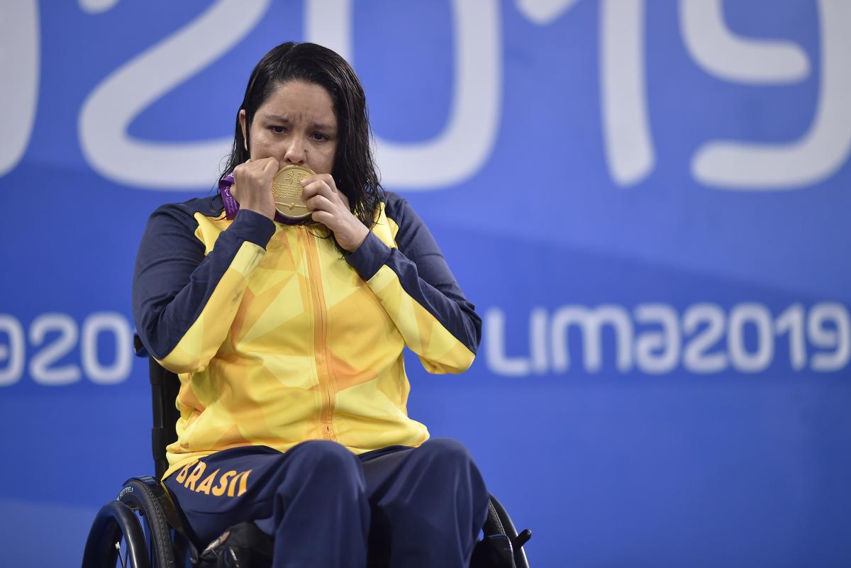 A woman in a wheelchair kissing a gold medal