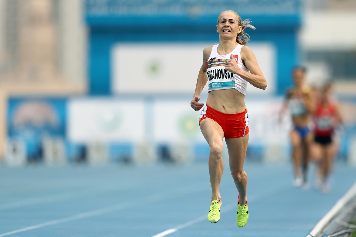 A female runner wearing Poland's uniform running on a blue track