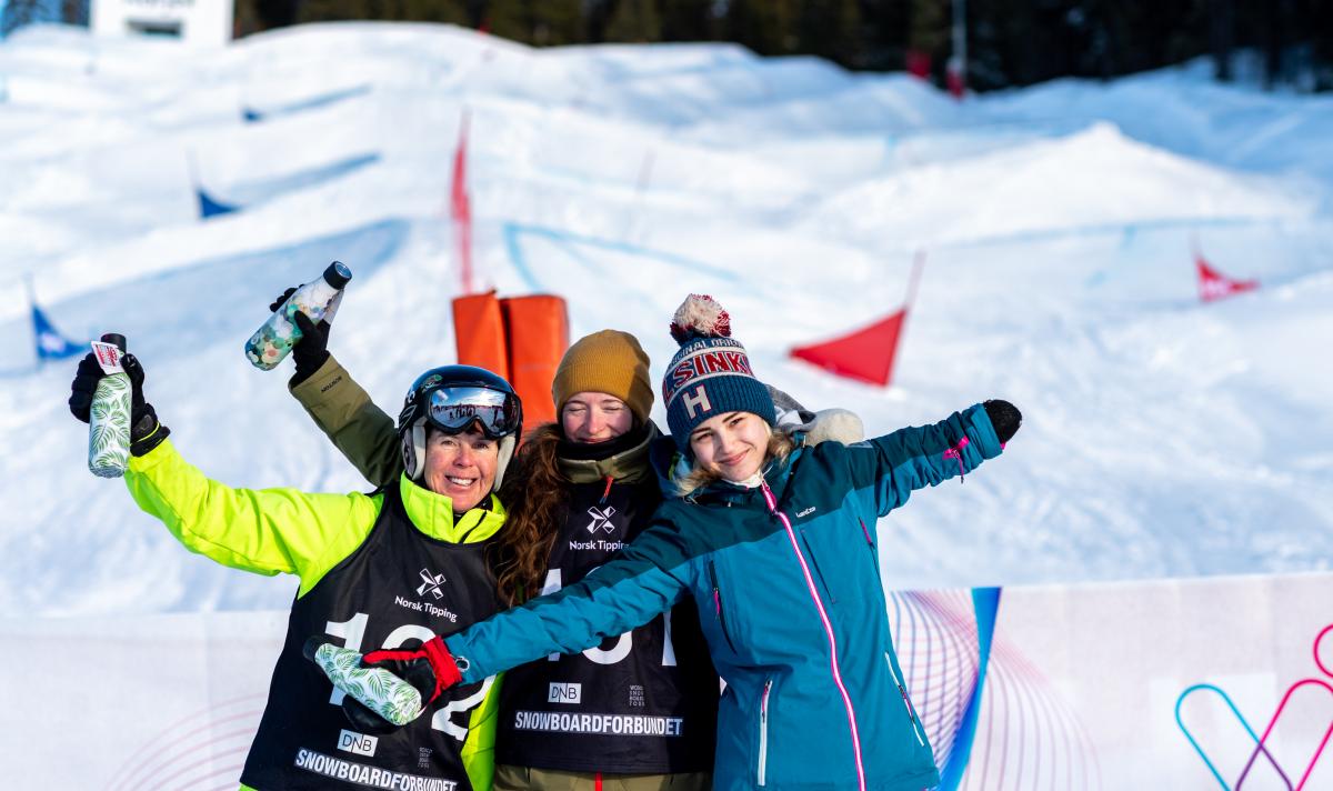 Three female Para snowboarders hugging and posing for a picture