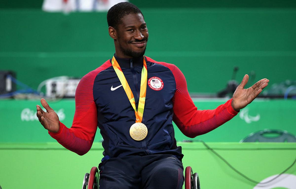 Black male in wheelchair smiling with gold medal around his neck