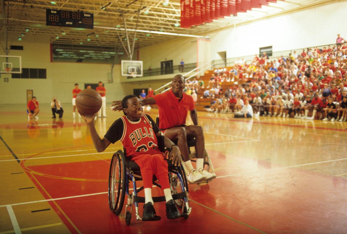 Boy in wheelchair holds basketball while Michael Jordan tries to block