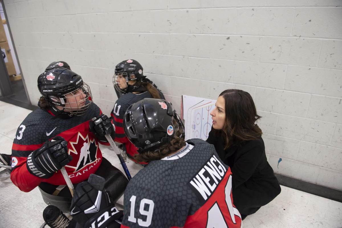 A woman talking to two women in hockey sledges