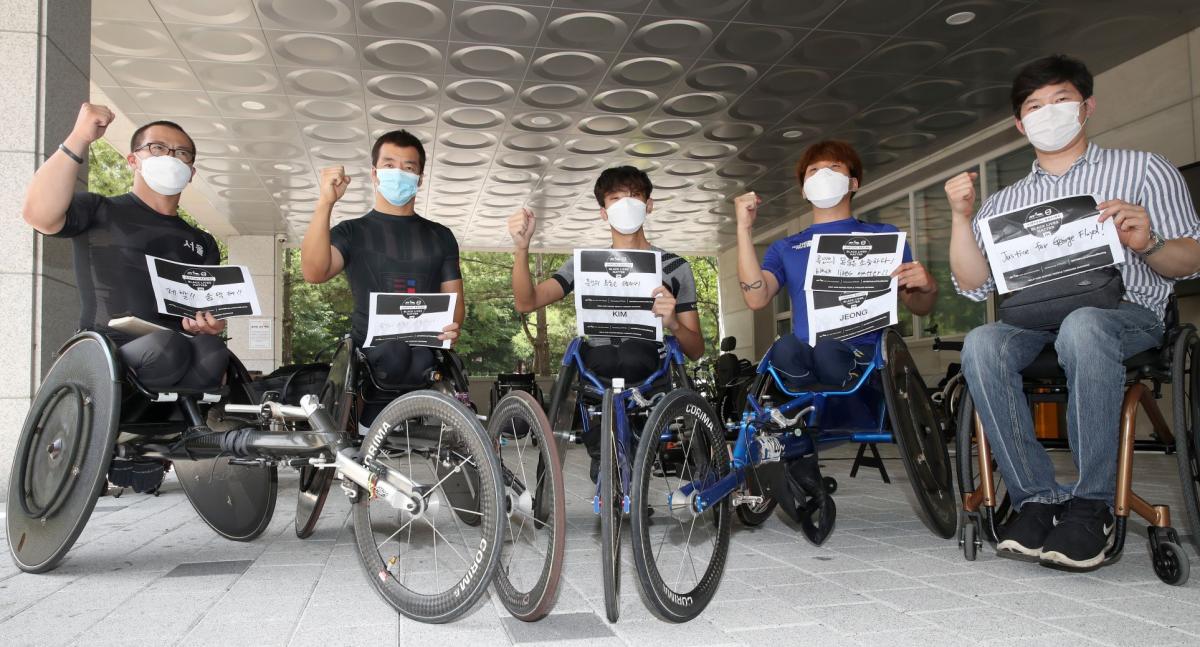 Five Korea wheelchair racers hold fists up with signs supporting Black Lives Matter