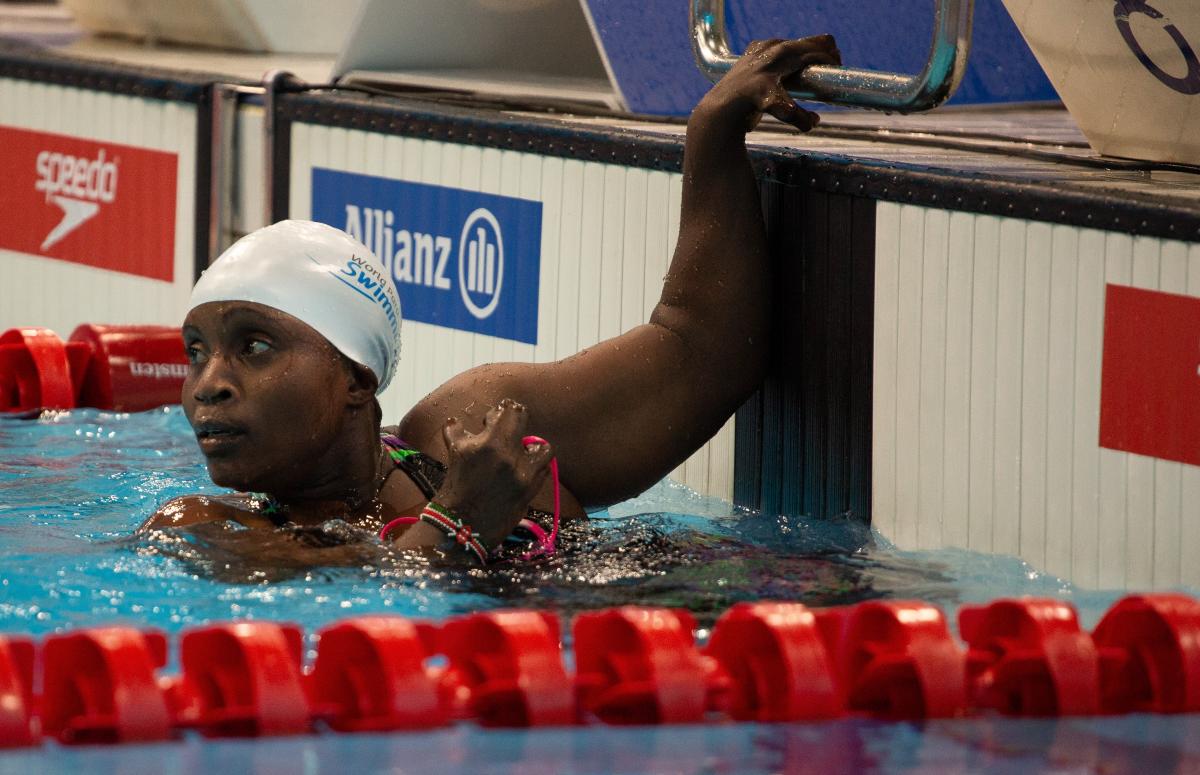 A female swimmer with her left hand on the board looking towards the  pool