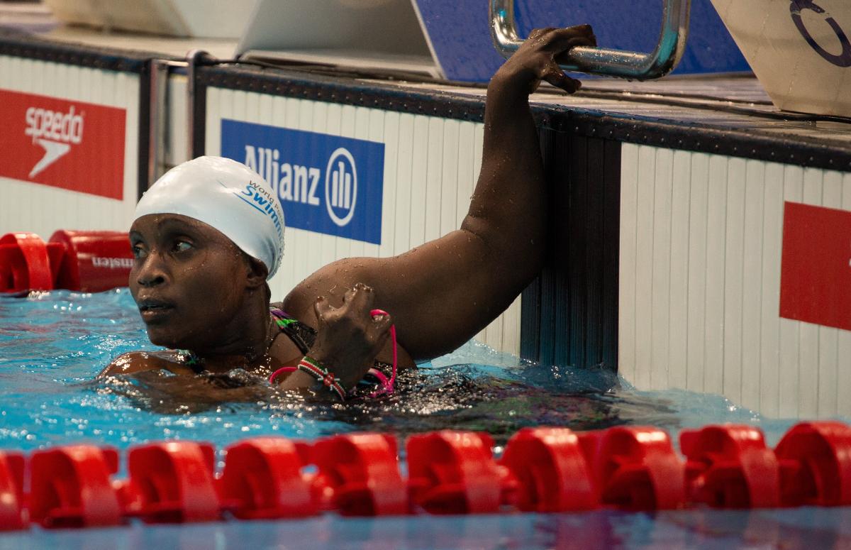 A female swimmer with her left hand on the board looking towards the pool