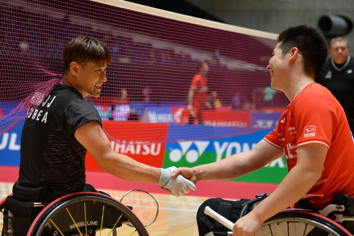 Two male Asian badminton players in wheelchairs shake hands