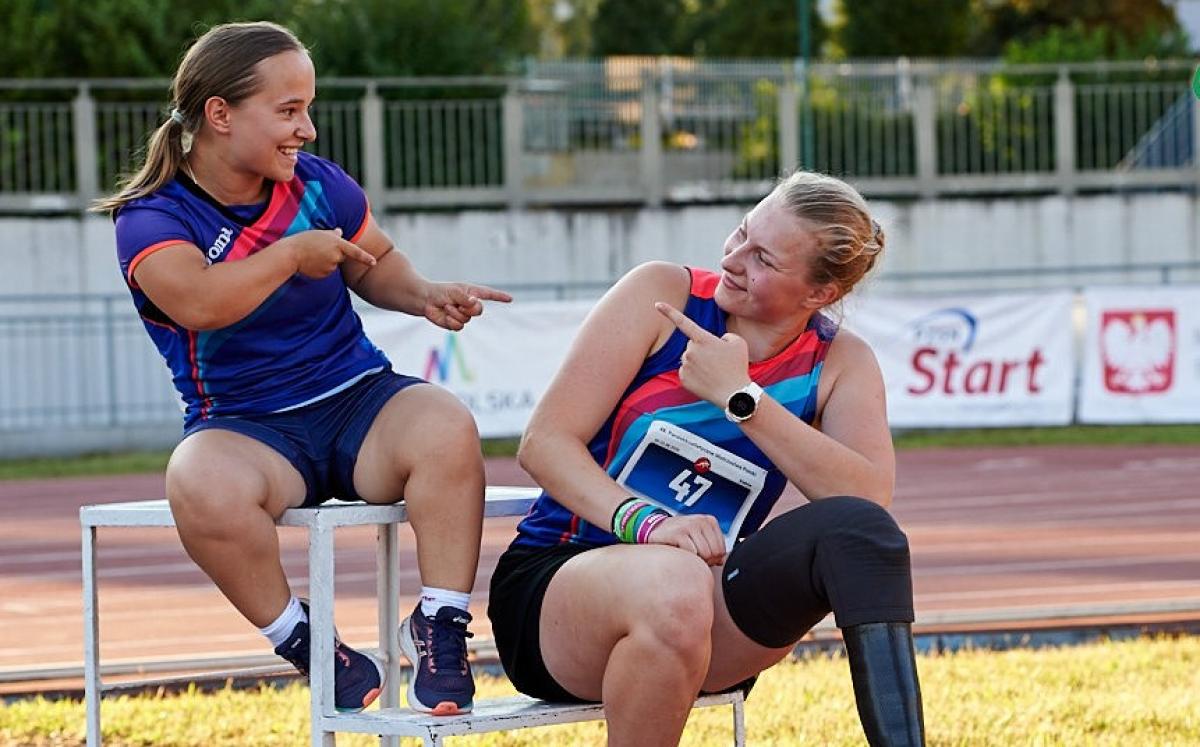 A short stature woman and a woman with a prosthetic leg point at each other