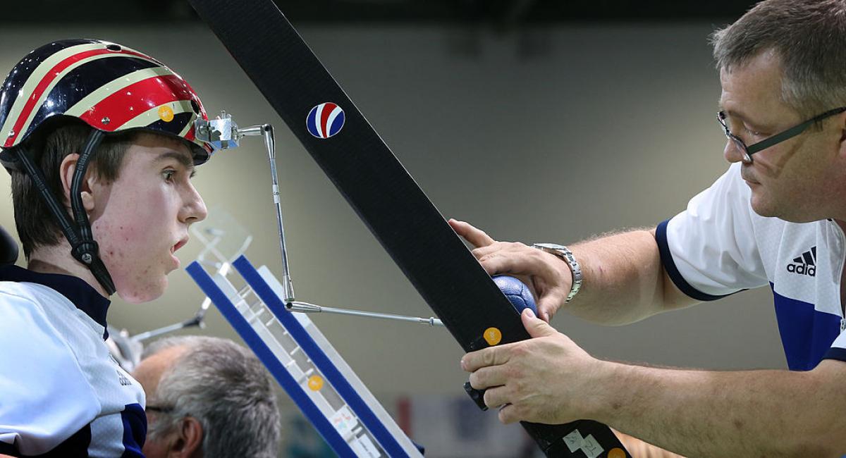 El atleta masculino de Boccia usa un puntero para golpear la pelota con su asistente ajustando la rampa