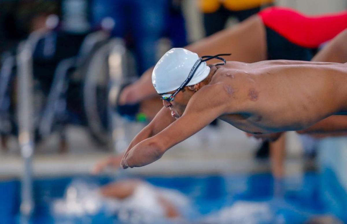 A man without his arms jumping in the swimming pool with another man behind him