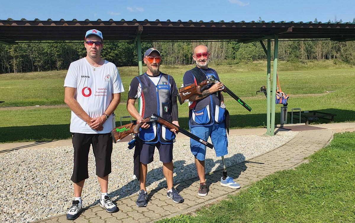 Three men standing on a shooting range, two of the holding shotguns