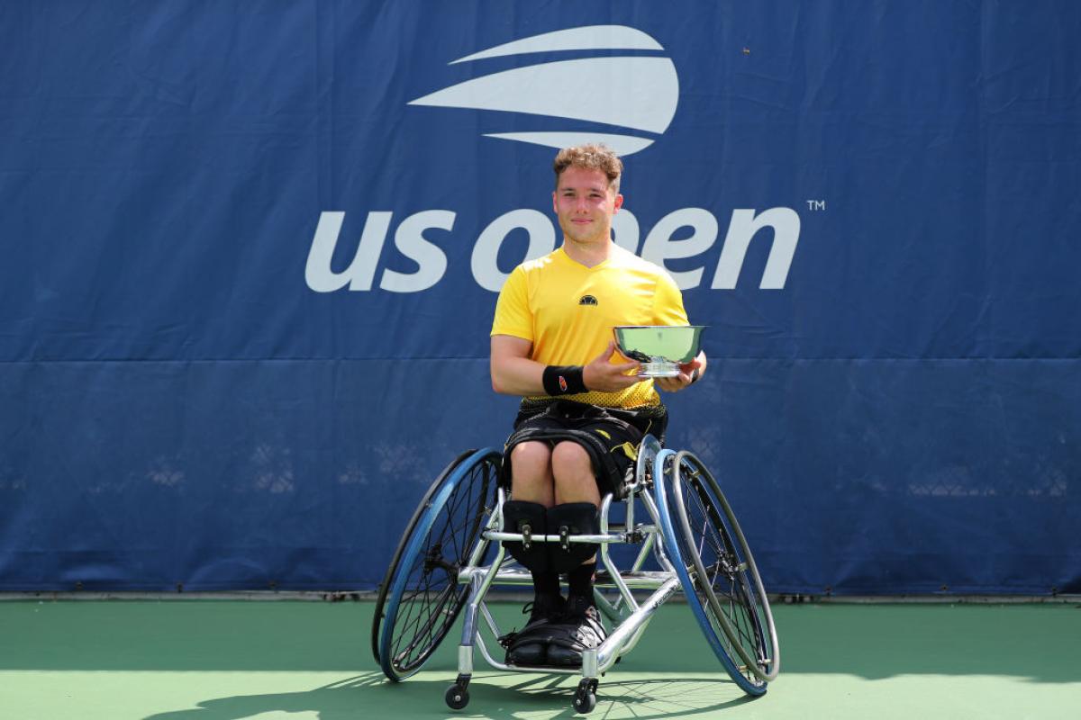 British male wheelchair tennis player smiles holding trophy