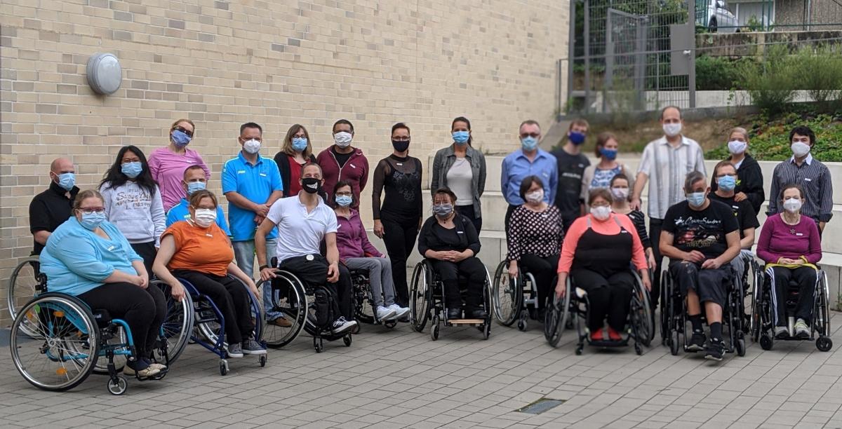 A group of wheelchair users outdoors with a group of standing people behind them