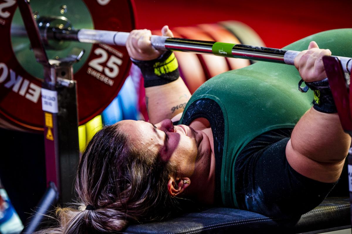 A short-stature woman lifting a bar on a bench press