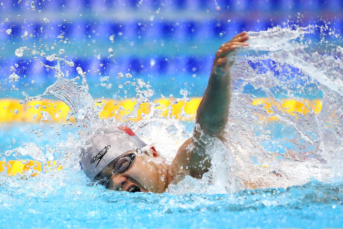 A man with a grey cap swimming in a pool