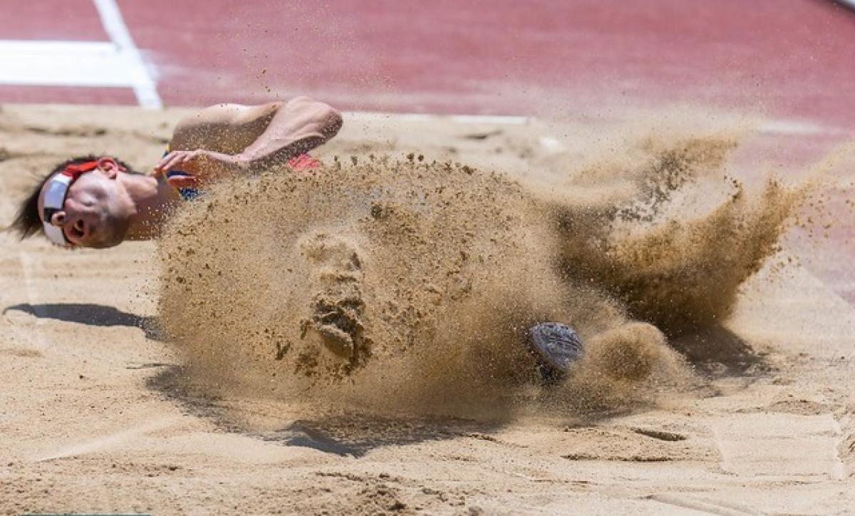 A man with a blindfold landing in a sand pit of a long jump track
