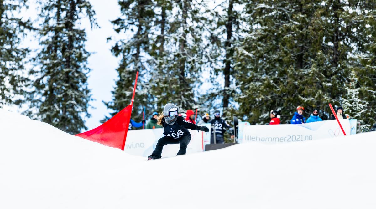 A female snowboarder competing being observed by a group of eight people 