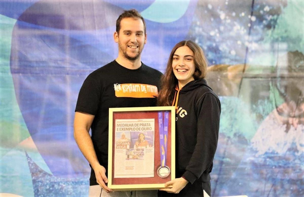 A man and a young woman smiling and holding a frame with a newspaper page and a medal