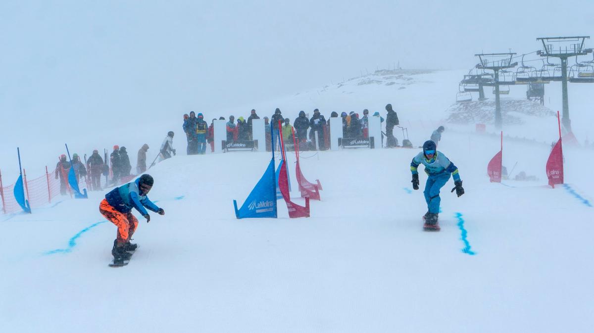 Two male Para snowboarders competing with a group of people watching in the background