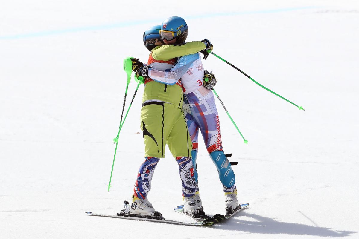 Two male alpine skiers hugging each other on the snow