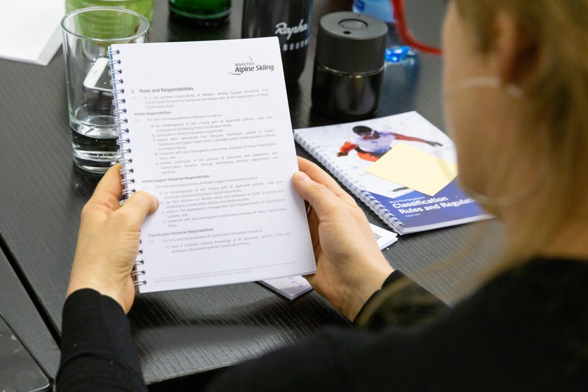 A woman reading a notebook with a World Para Alpine Skiing logo