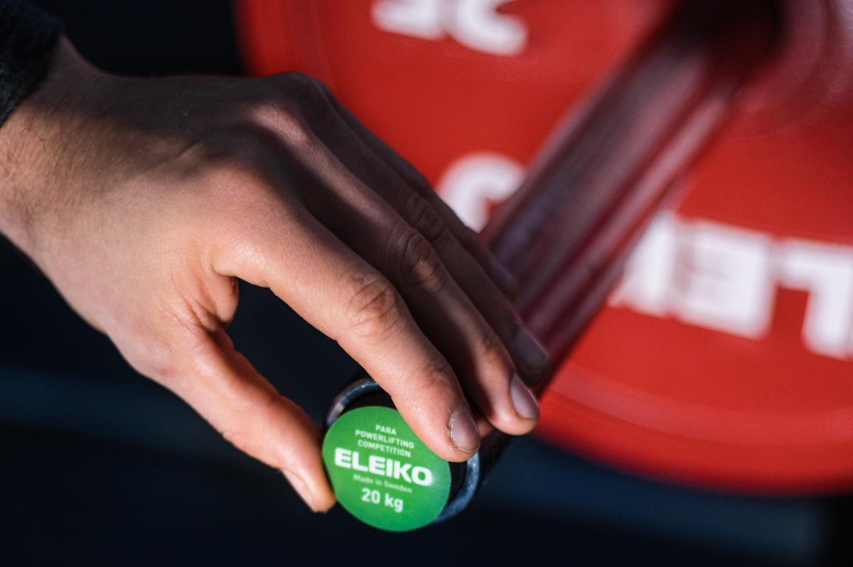 A male hand plugging a green Eleiko sensor on a barbell