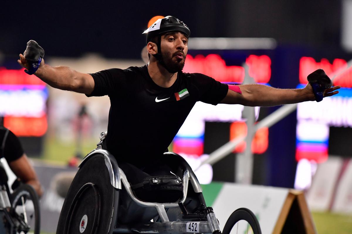 A man in a racing wheelchair celebrating with his arms stretched 