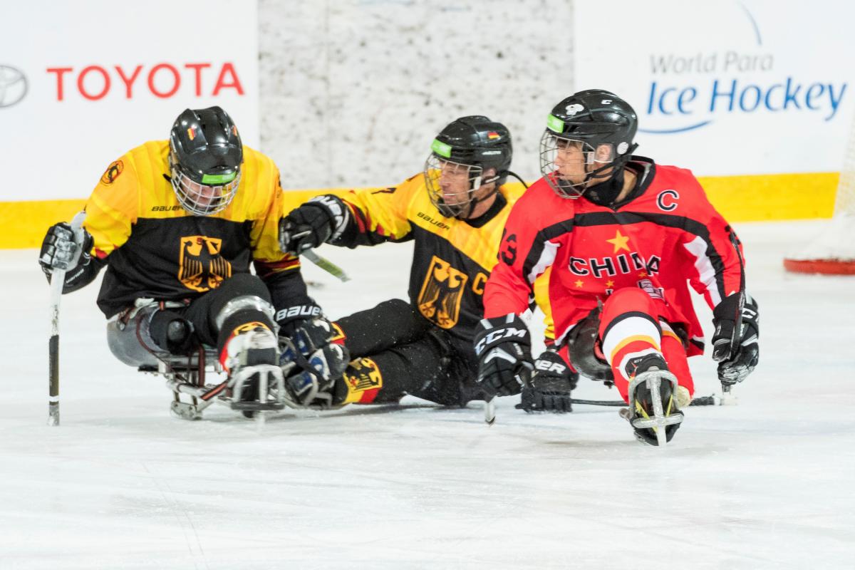 A man with the Chinese uniform on an ice sledge competing against two other men wearing Germany's uniform