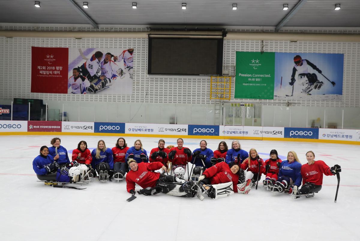 A group of 17 women on sledges wearing read and blue uniforms on an ice rink 