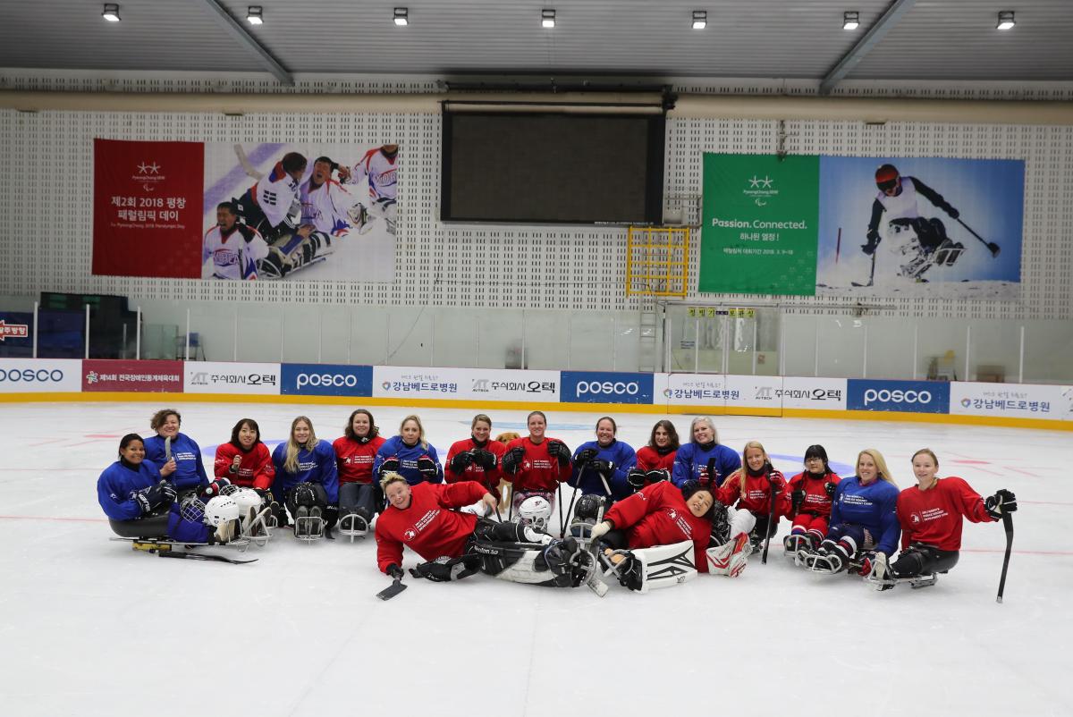 A group of 17 women on sledges wearing read and blue uniforms on an ice rink