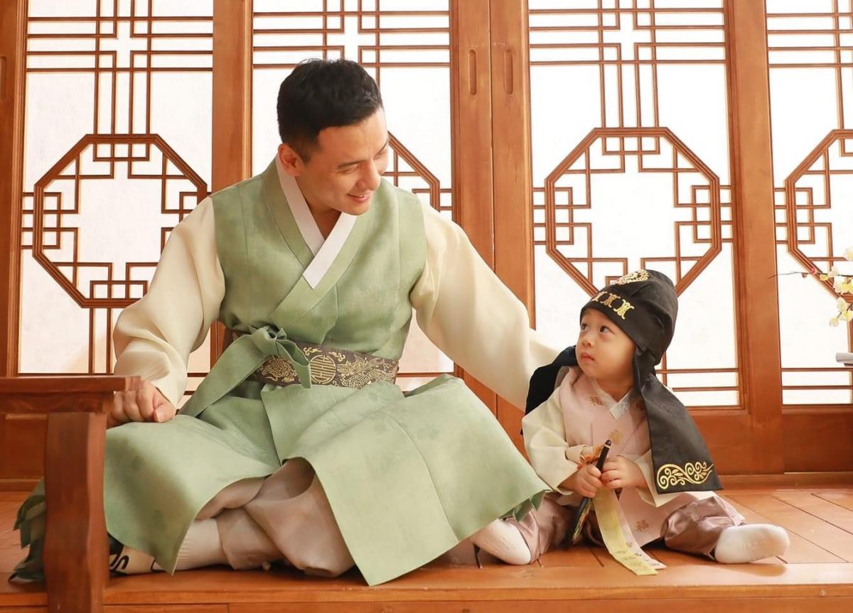 A man in typical Korean clothes looking at a baby on the floor