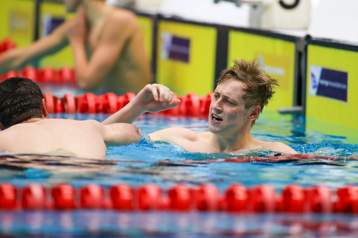 A male swimmer celebrating near another swimmer seeing from behind in a swimming pool