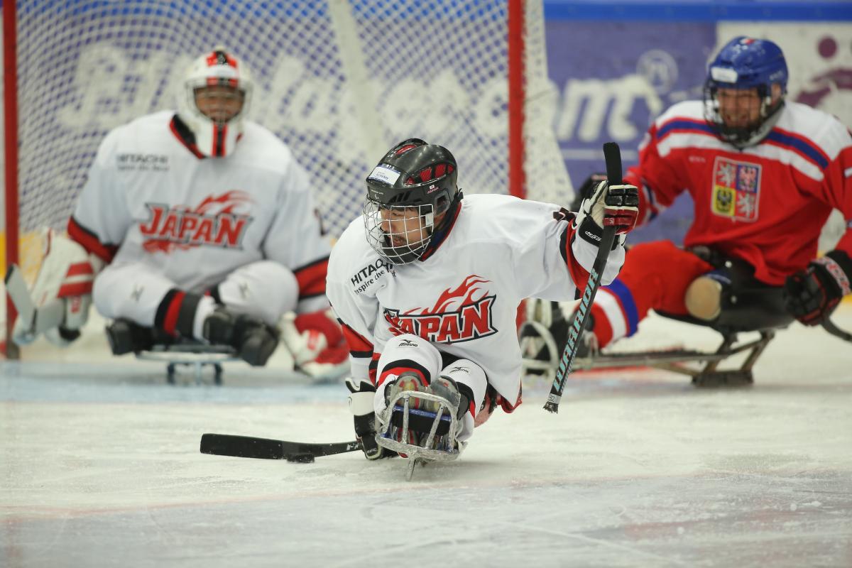 A sledge hockey player from Japan on an ice rink with Japan's goaltender and a Czech Republic player in the background