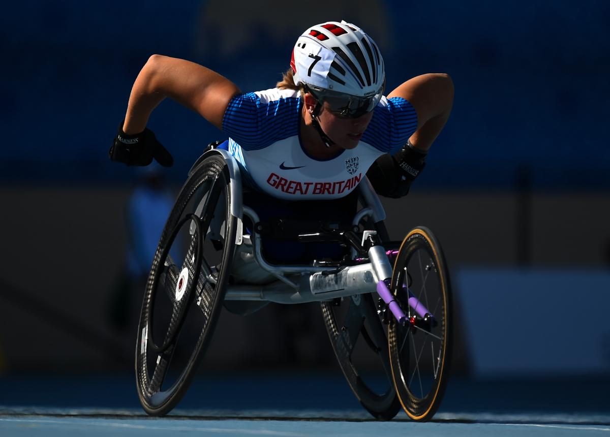 A female athlete competing in a wheelchair race in a blue track