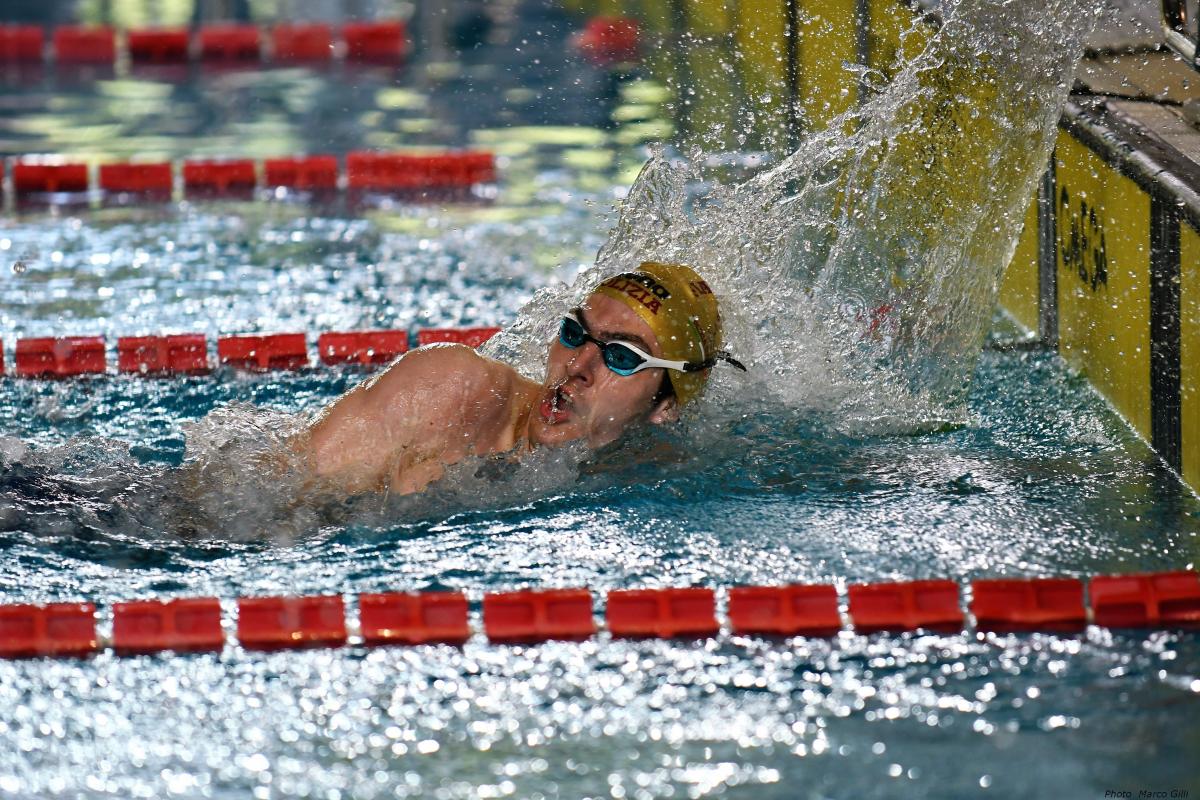 A male swimmer finishing his race in a swimming pool